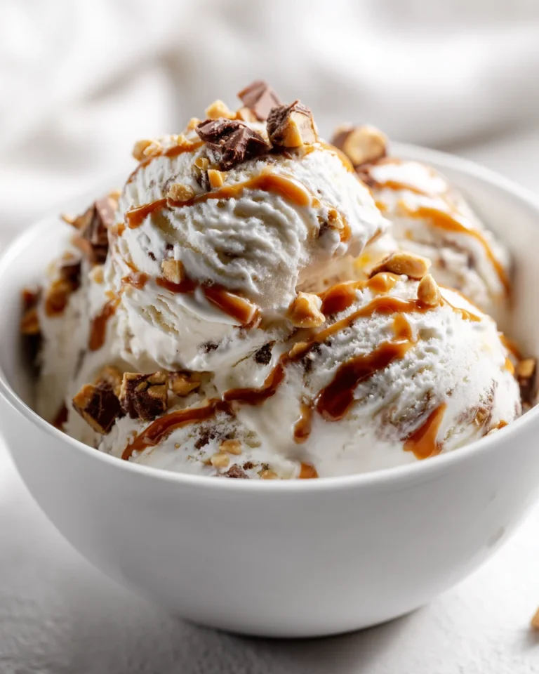 Homemade vanilla ice cream topped with chopped Snickers bars and caramel drizzle in a white porcelain bowl