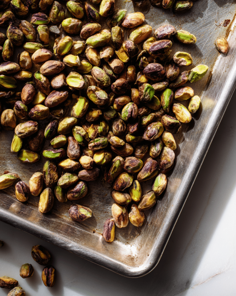 Roasted pistachio nuts spread across a metal baking sheet