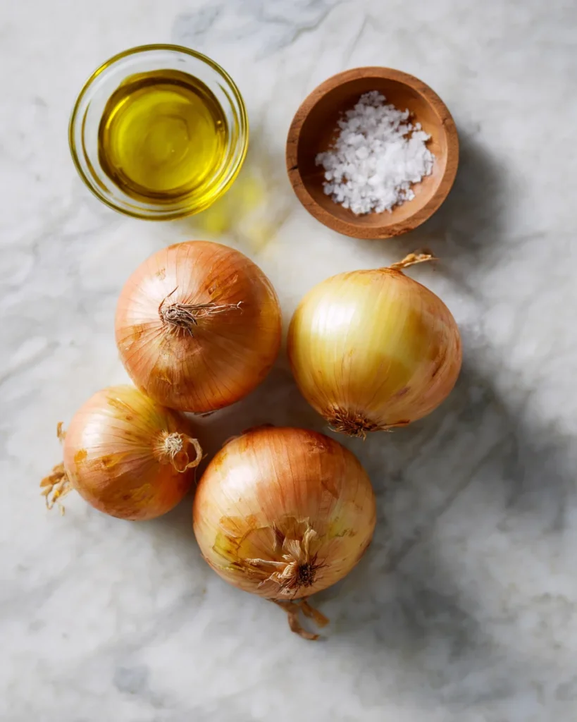 Whole onions, olive oil, and sea salt on a marble countertop