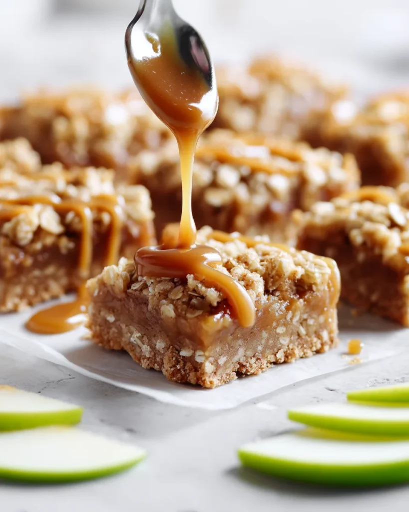 Spoon drizzling warm salted caramel over an apple crumb bar, green apple slices nearby, bright daylight.	