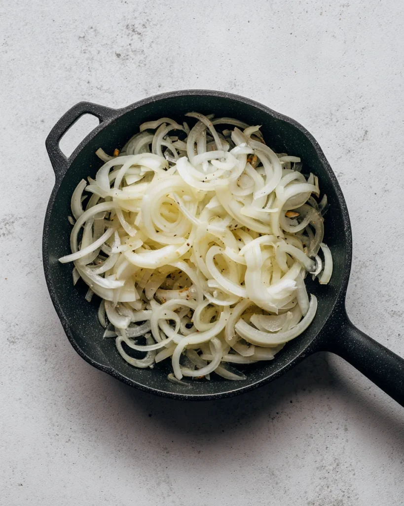 Thinly sliced raw onions in a skillet, ready for caramelizing